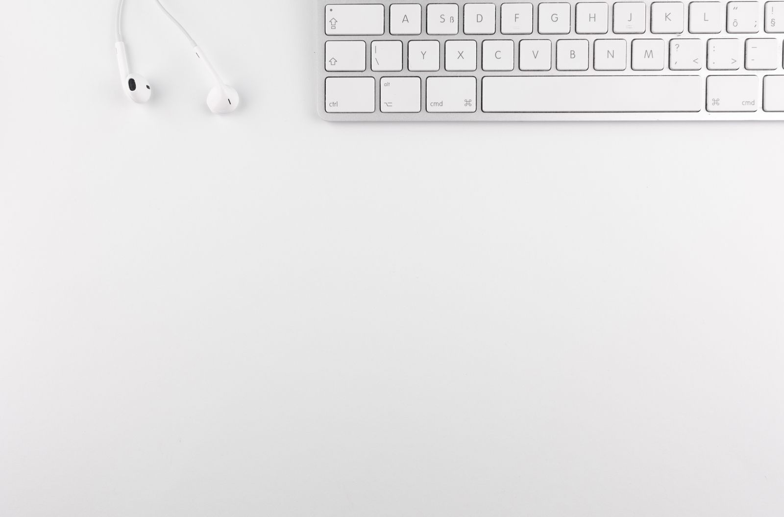 Vista de cima de um teclado branco e fones de ouvido sobre uma mesa branca.